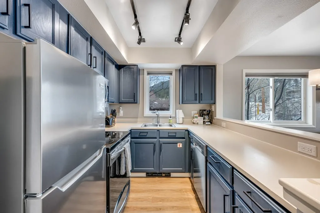 A kitchen with blue cabinets, stainless steel appliances, and windows.