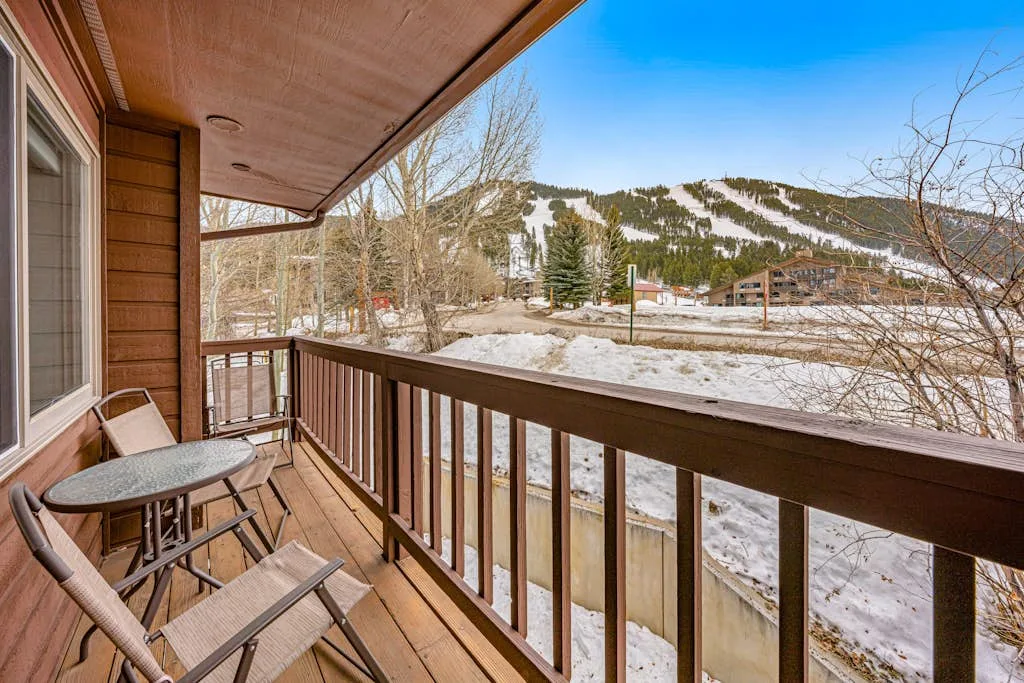 A wooden balcony overlooks a snowy landscape and forested mountain.