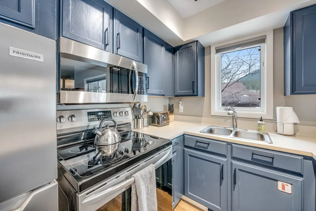 A kitchen with blue cabinetry, stainless steel appliances, and a window above the sink.