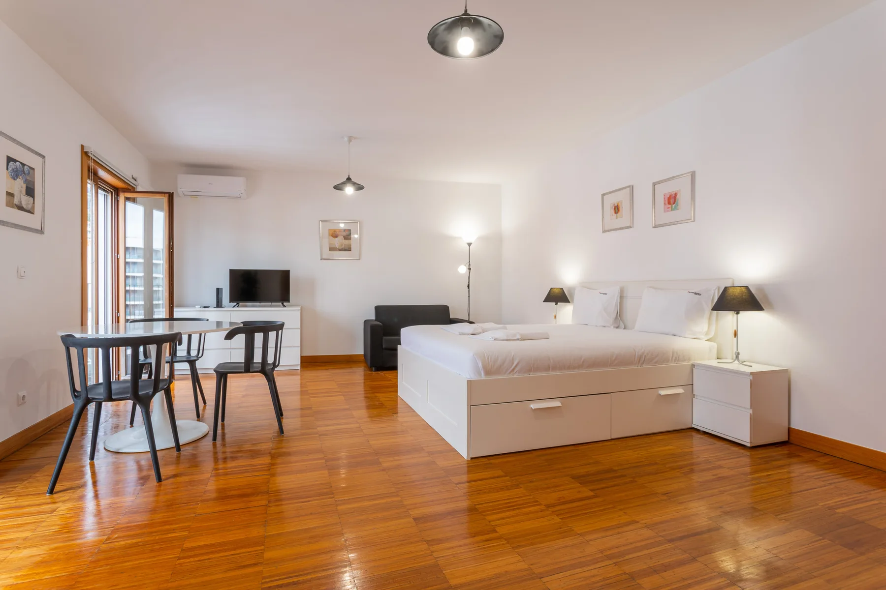 A bedroom and dining area share an open room with polished wood flooring.