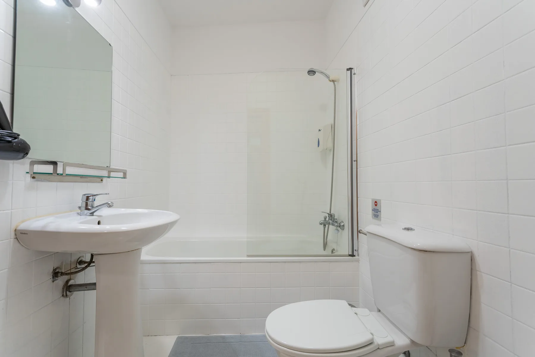 Un baño alicatado con lavabo, espejo, inodoro y ducha.