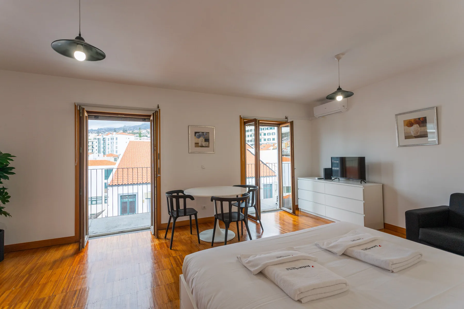A studio room with a dining table, bed, and balcony doors.