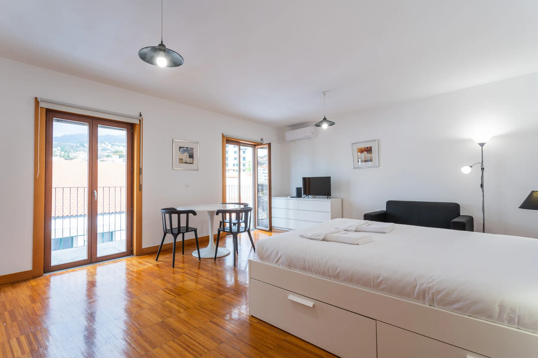 A studio bedroom with a bed, small dining area, and balcony doors.