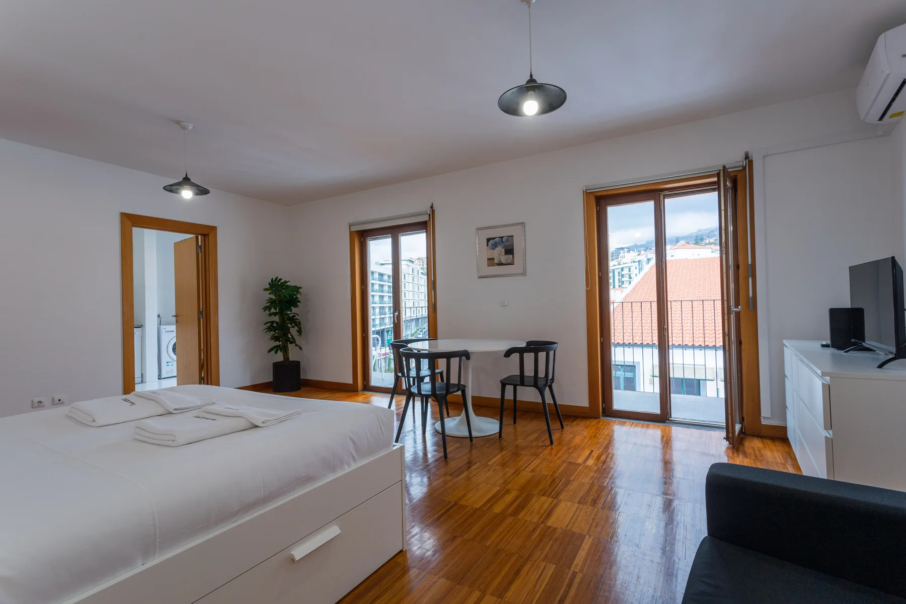 A bright studio bedroom and seating area open onto a balcony through glass doors.