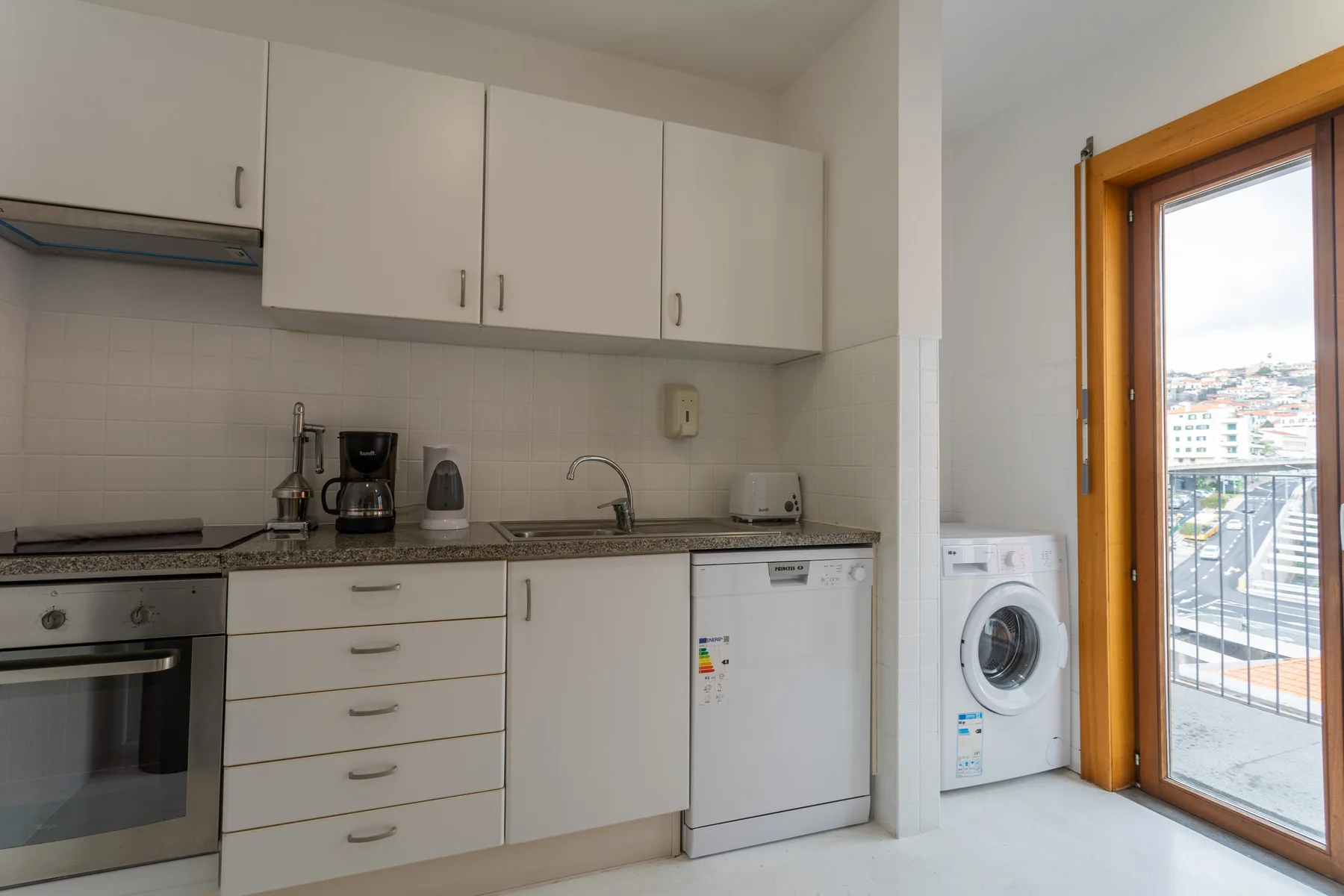 A compact kitchen with white cabinets and a glass door opening onto a balcony.
