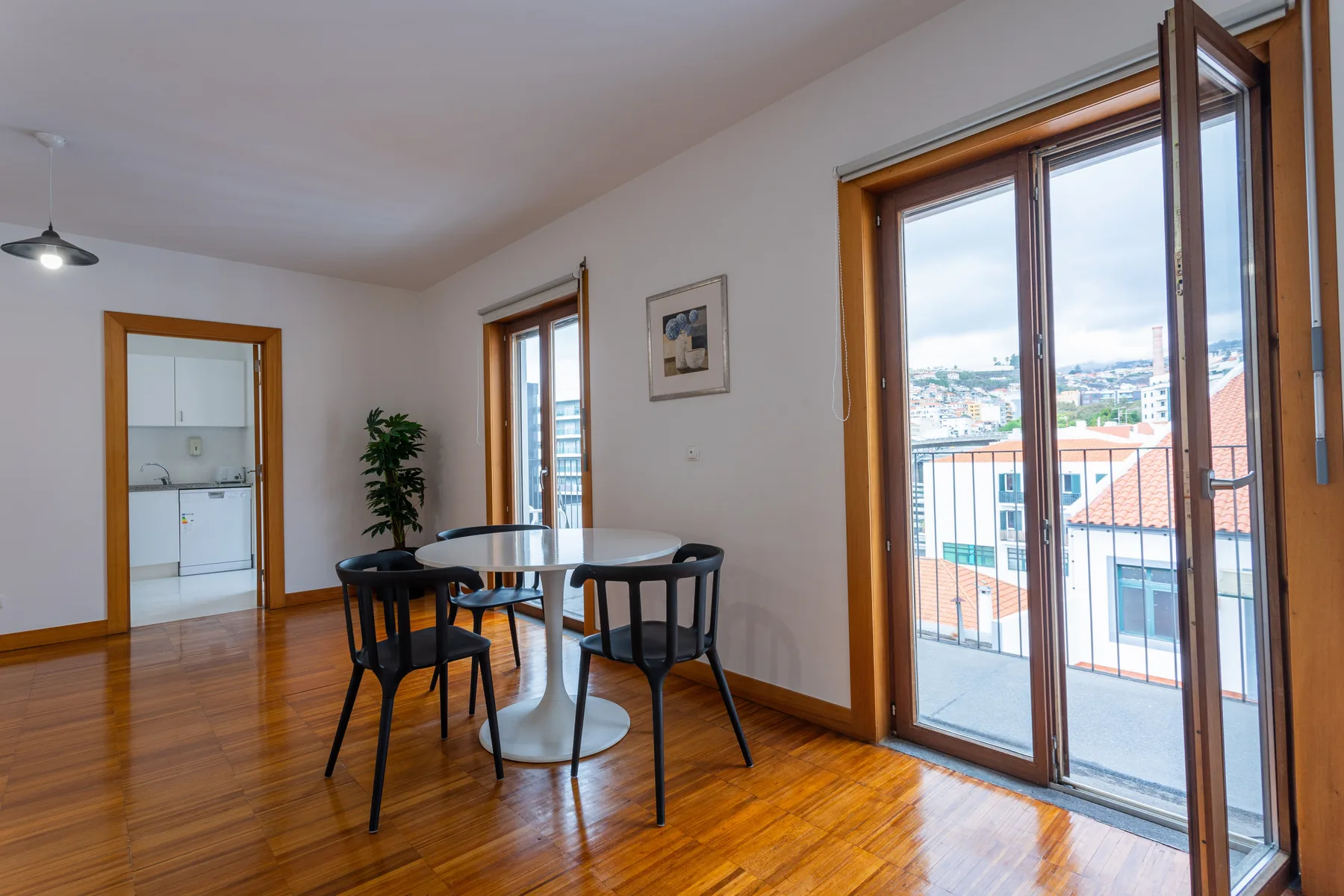 A dining area with a table and chairs beside an open balcony door.