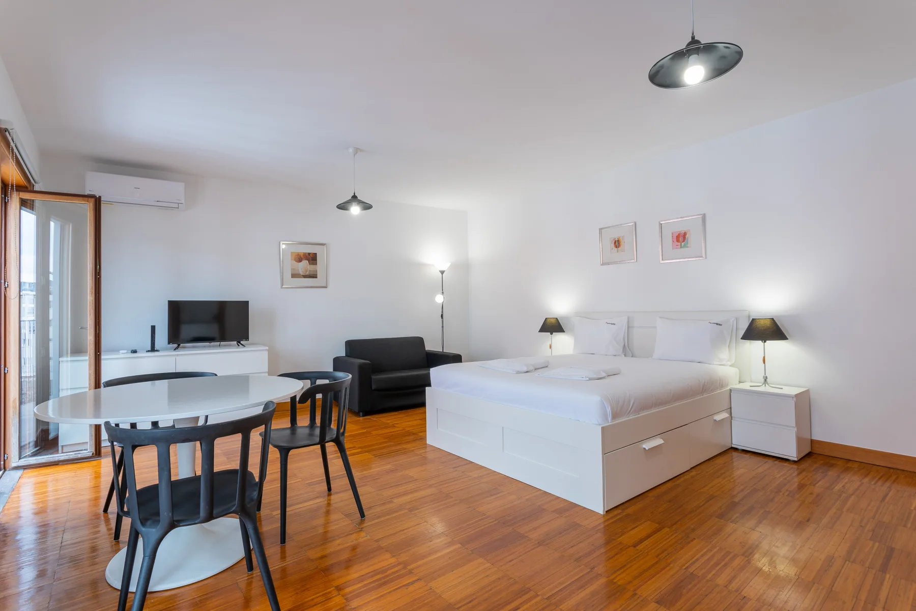 A studio room combines a bed, a small dining area, and a television.