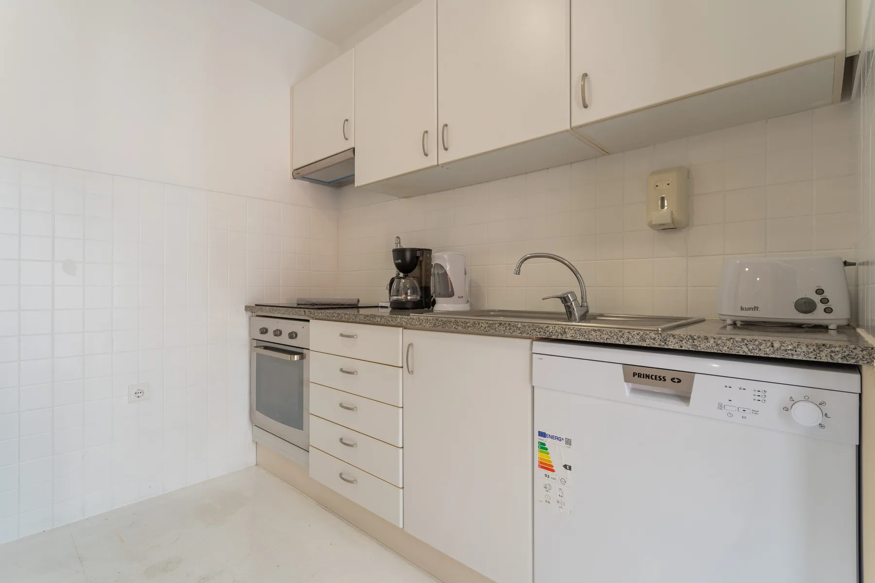 A compact kitchen with white cabinets, a countertop, and built-in appliances.