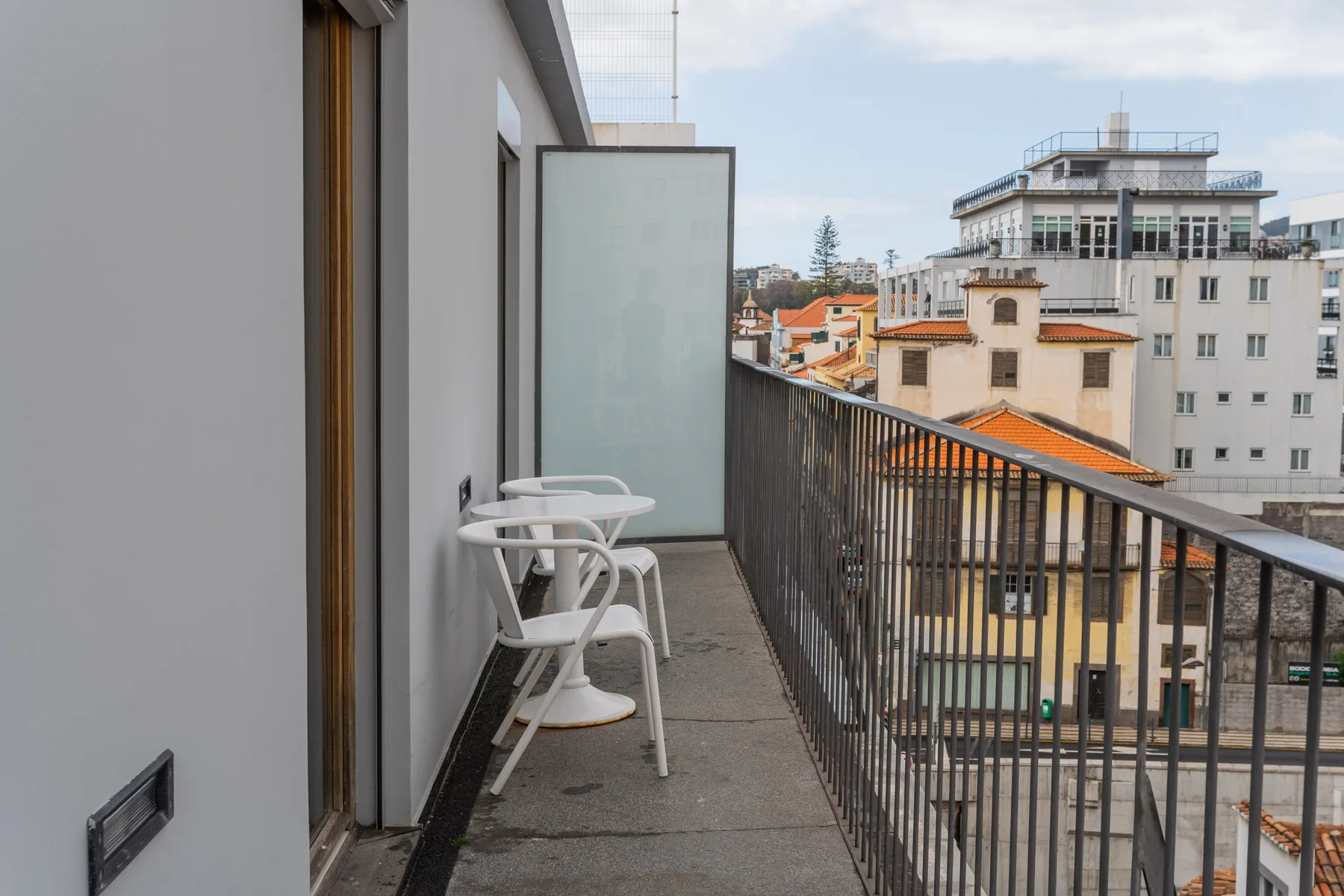 A narrow balcony with seating overlooks neighboring buildings and rooftops.