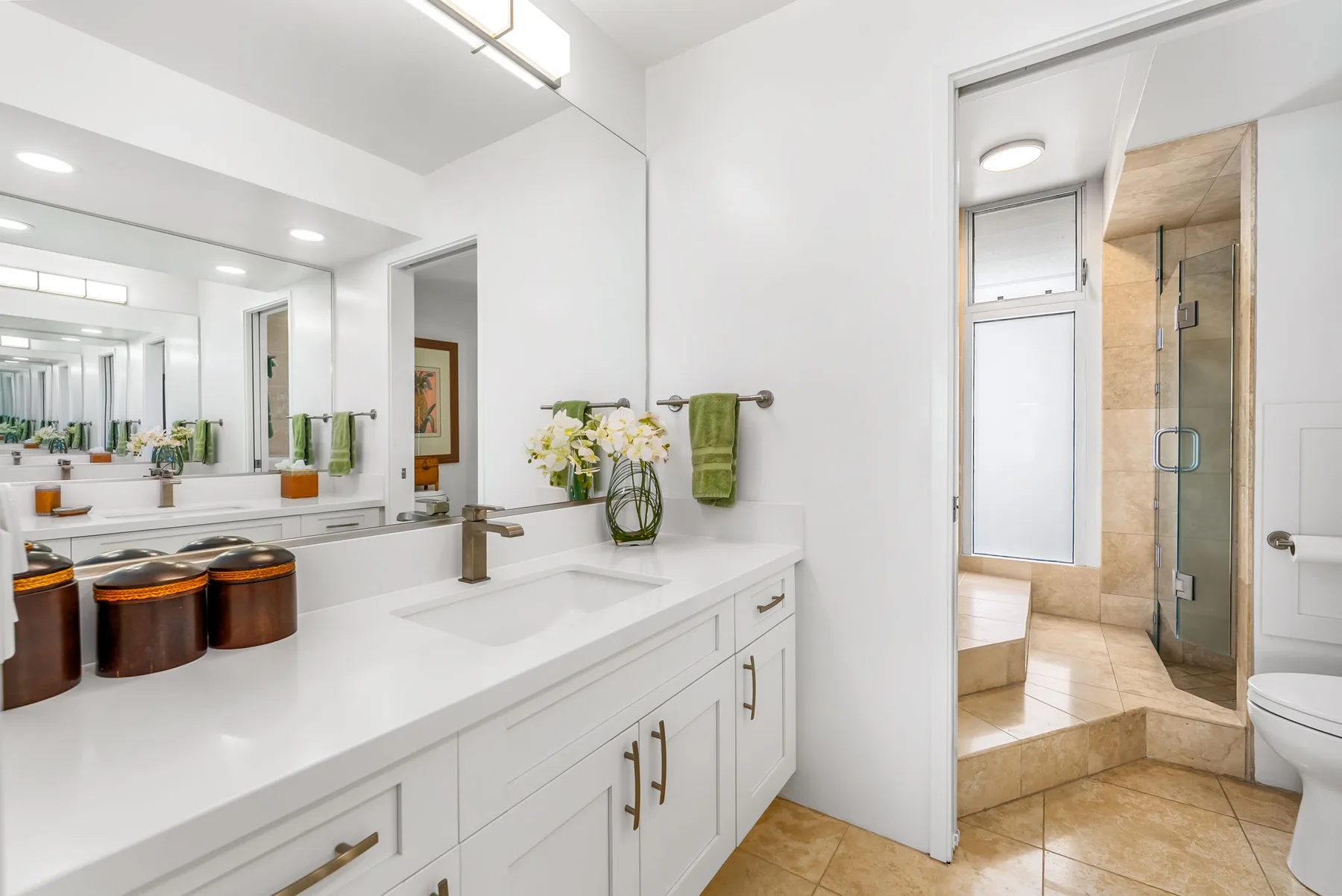 Un baño luminoso con un largo mueble blanco y una ducha de vidrio.