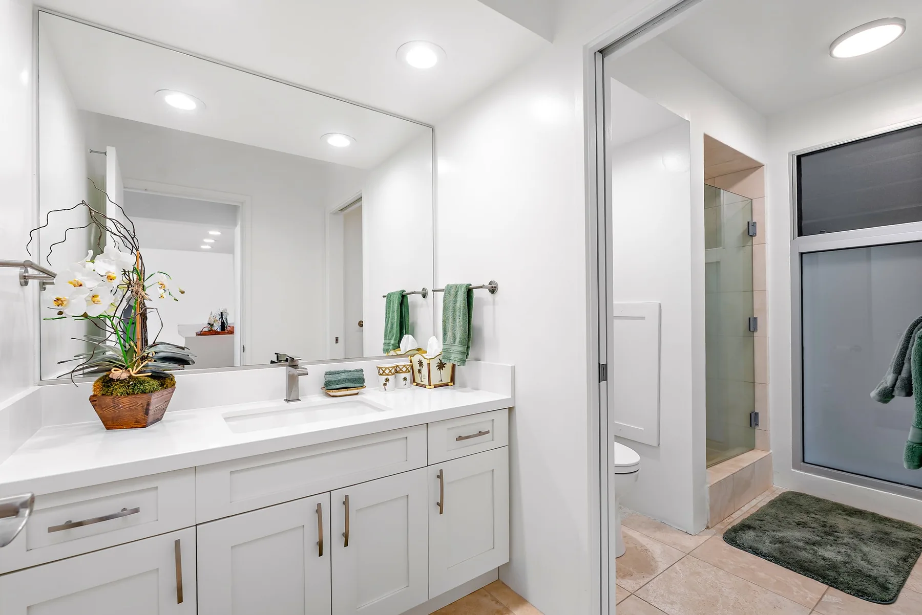 Un baño luminoso con un tocador largo, espejo de pared y ducha de vidrio.