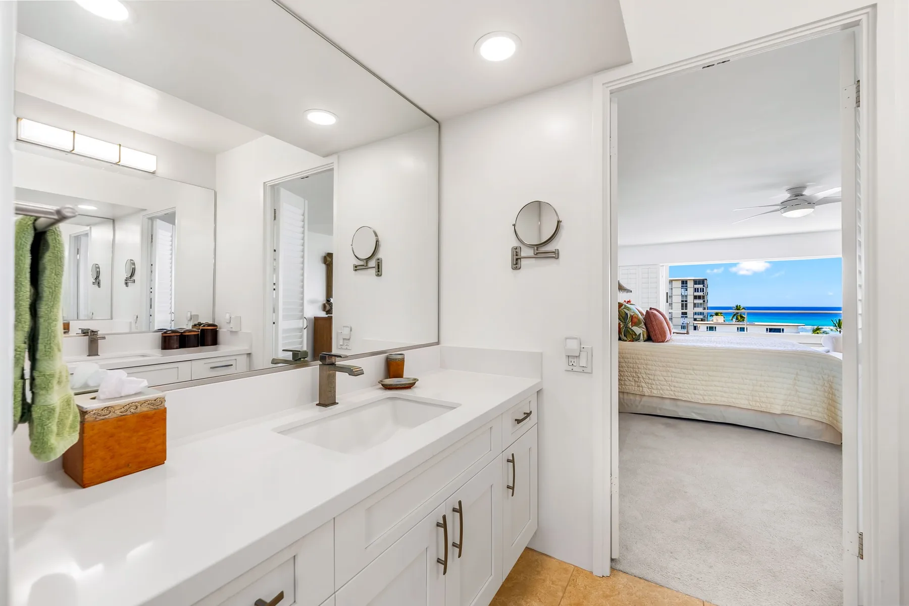 Un tocador de baño luminoso con un espejo grande da a un dormitorio.