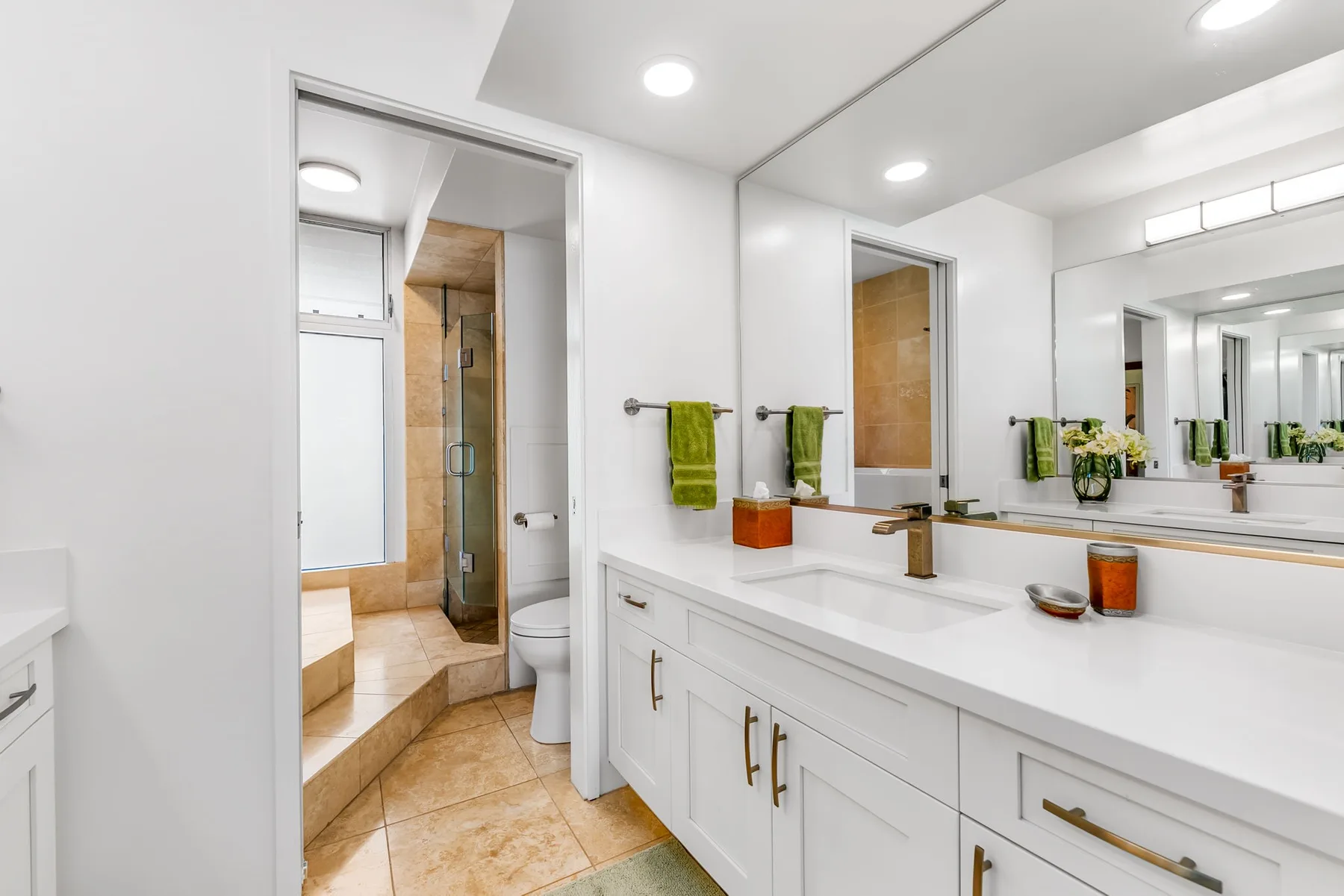 Un baño luminoso tiene un largo tocador con lavabos y un gran espejo de pared.