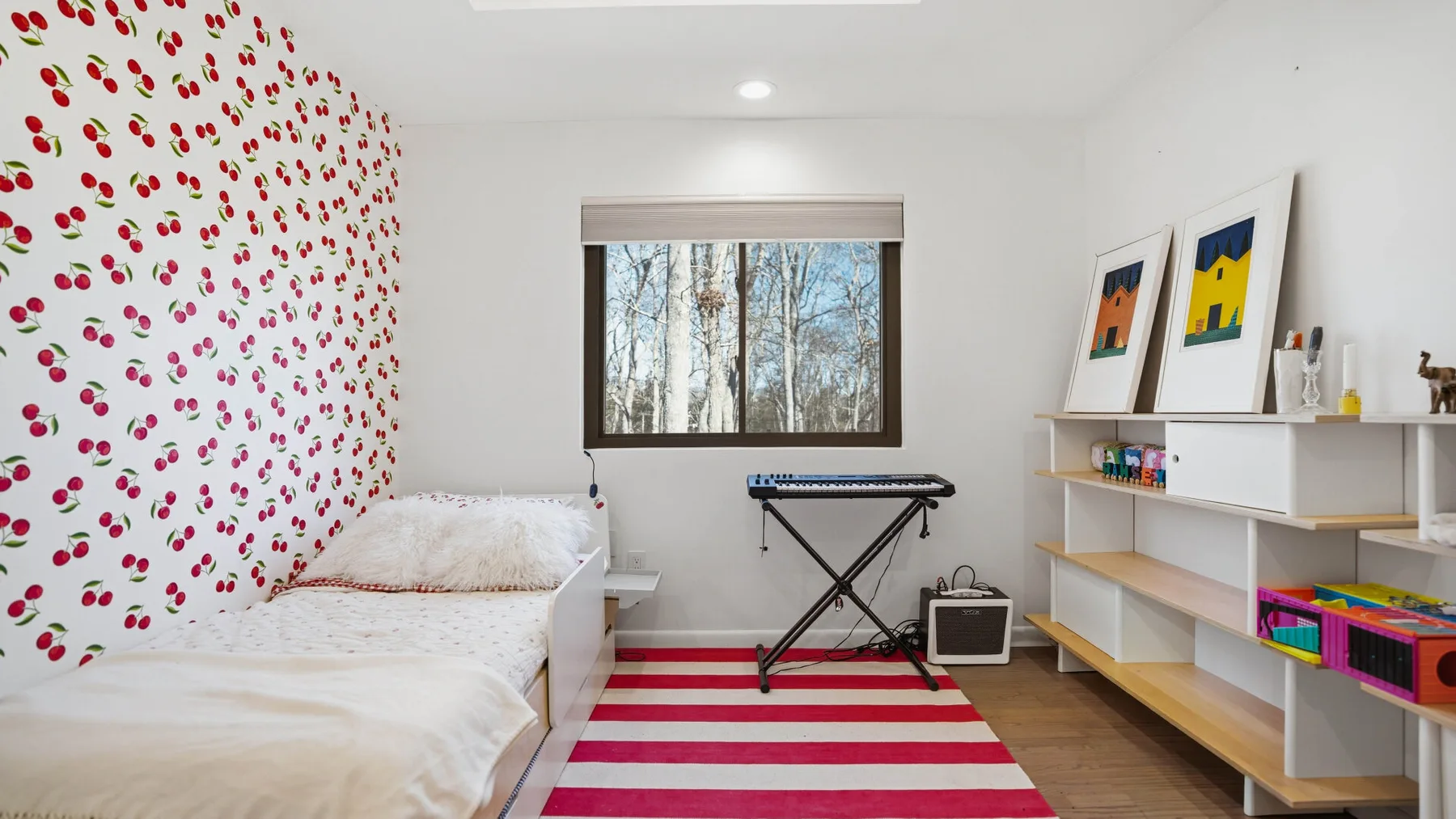 A bright bedroom has a bed beside a red-and-white striped rug.