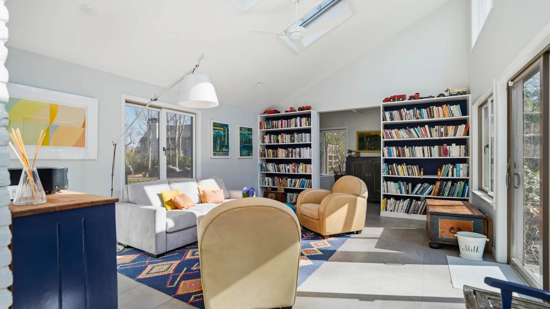 A bright living room with bookshelves, seating, and a colorful patterned rug.