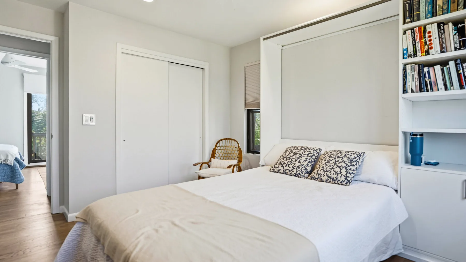 A bright bedroom with a neatly made bed and built-in shelving.
