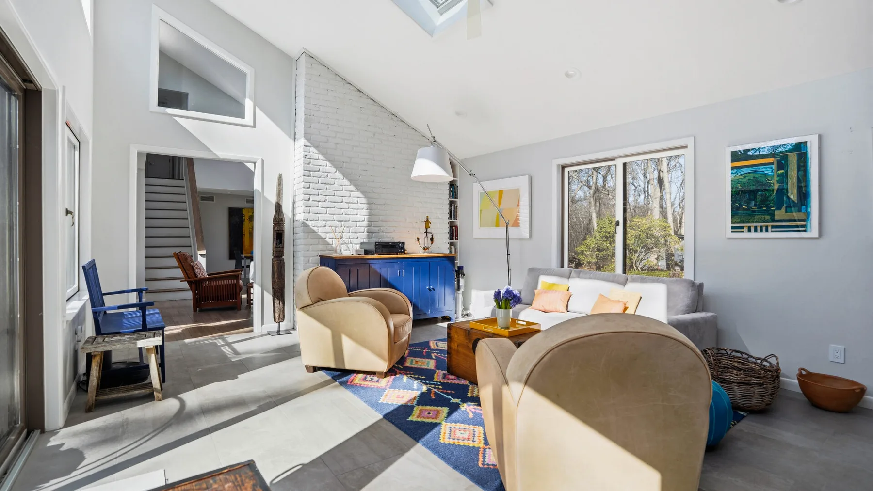 A bright living room with upholstered seating, a blue cabinet, and large windows.
