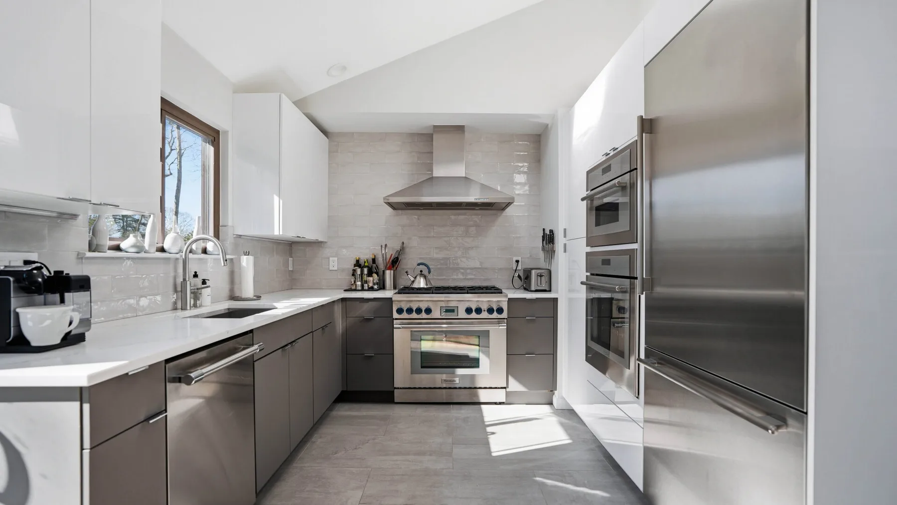 A modern kitchen with gray cabinetry, stainless steel appliances, and a central range.
