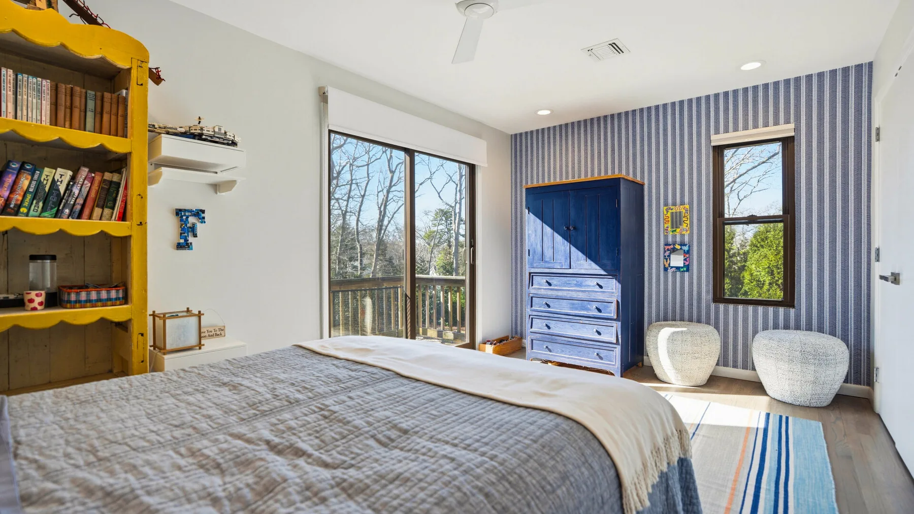 A bedroom with a large bed, blue dresser, and windows overlooking trees.