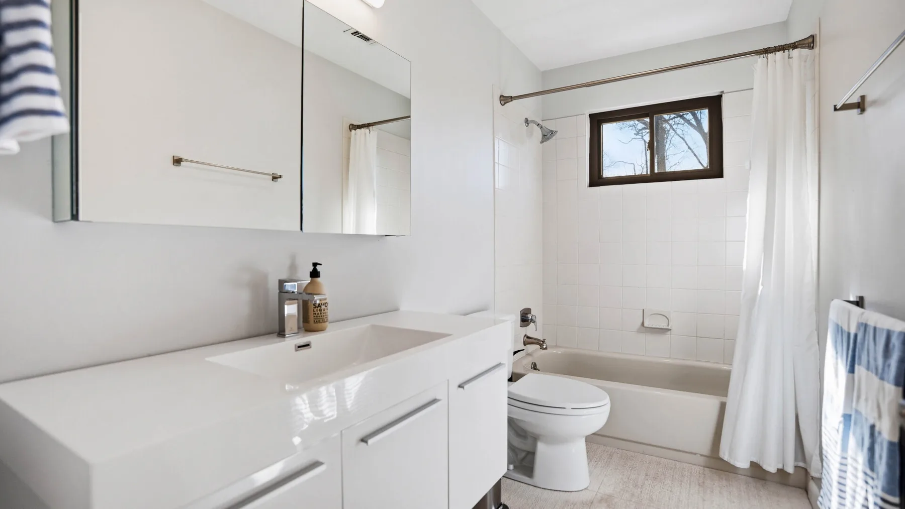 A bright bathroom with a sink, toilet, and bathtub beneath a window.