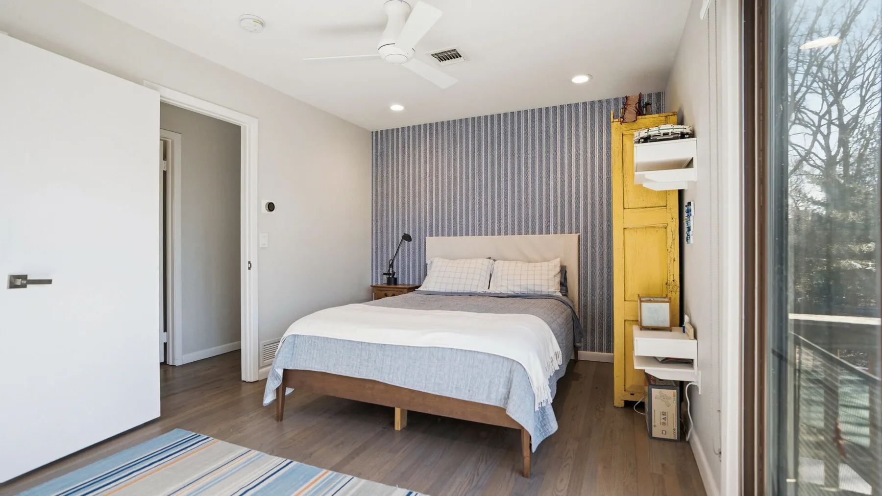 A bright bedroom with a neatly made bed and a large window.