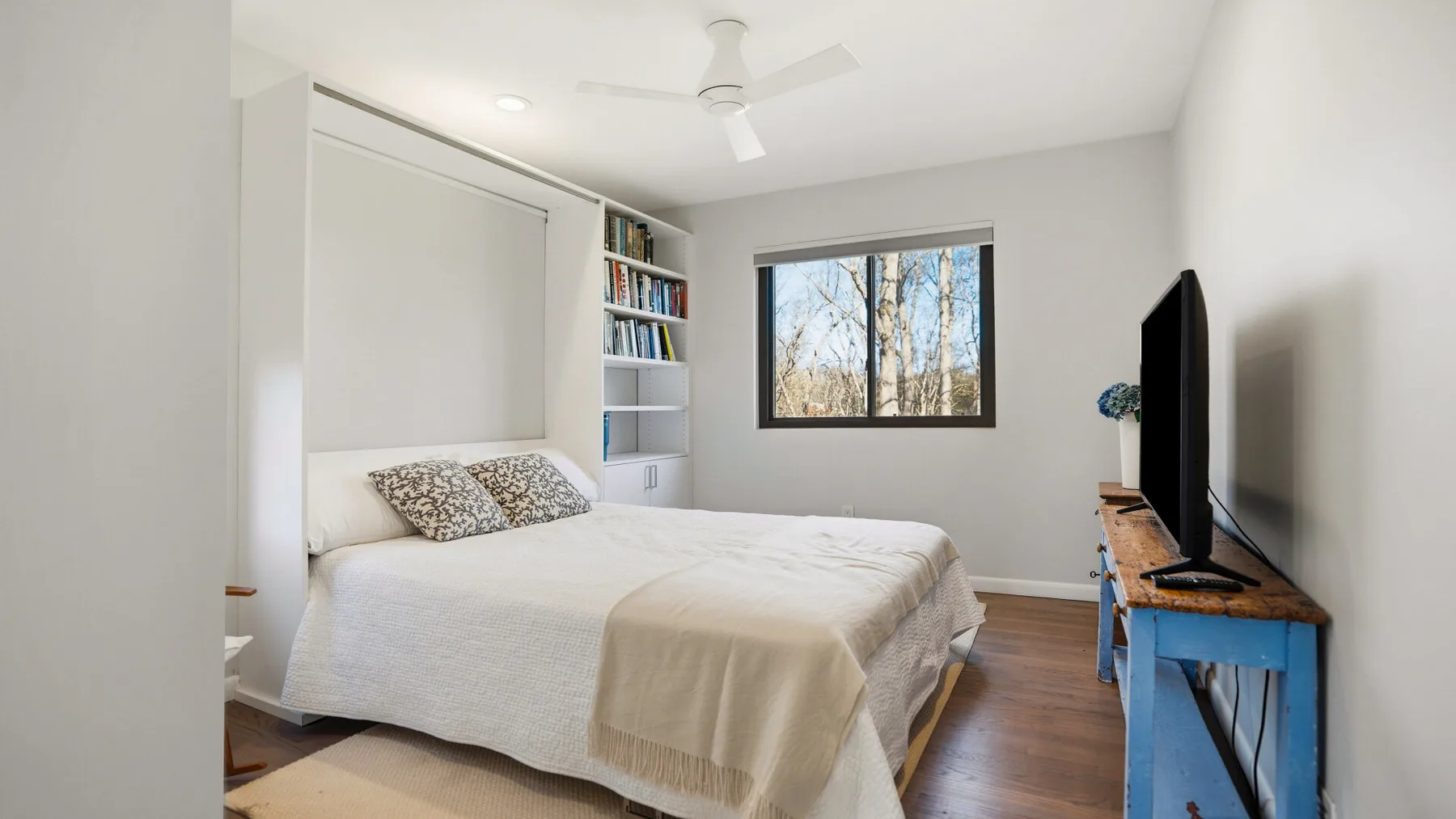 A bright bedroom with a neatly made bed and a large window.