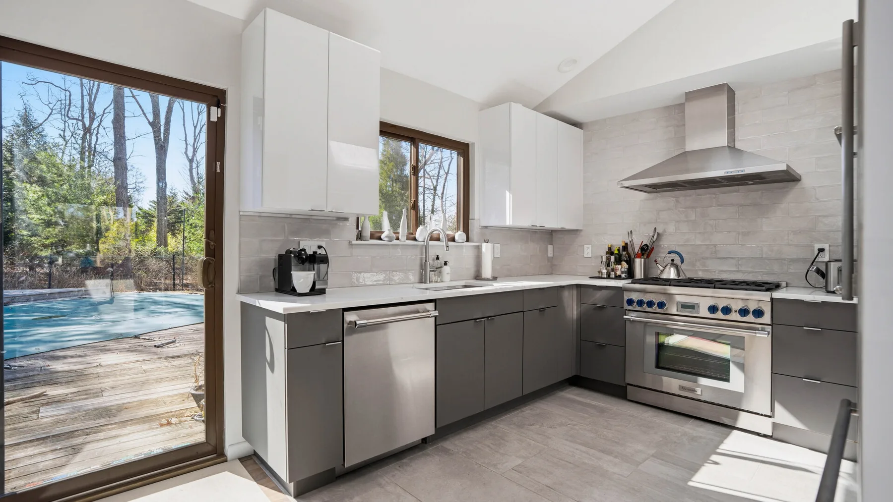 A modern kitchen with gray cabinets and large windows overlooking a pool.