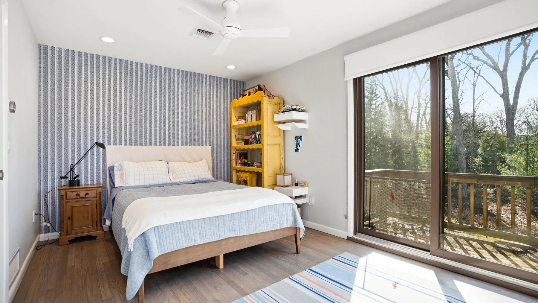 A bedroom with a bed, a bookcase, and sliding glass doors opening onto a balcony.