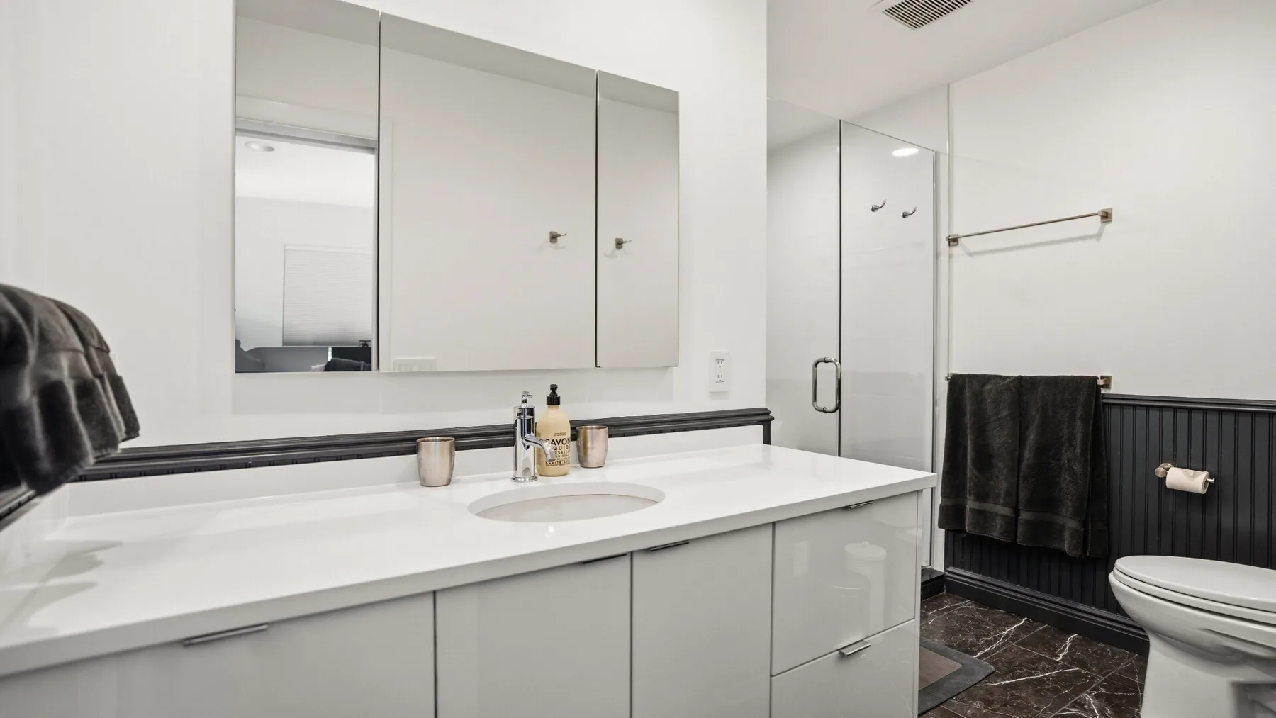A modern bathroom with a wide vanity, mirror, shower, and toilet.