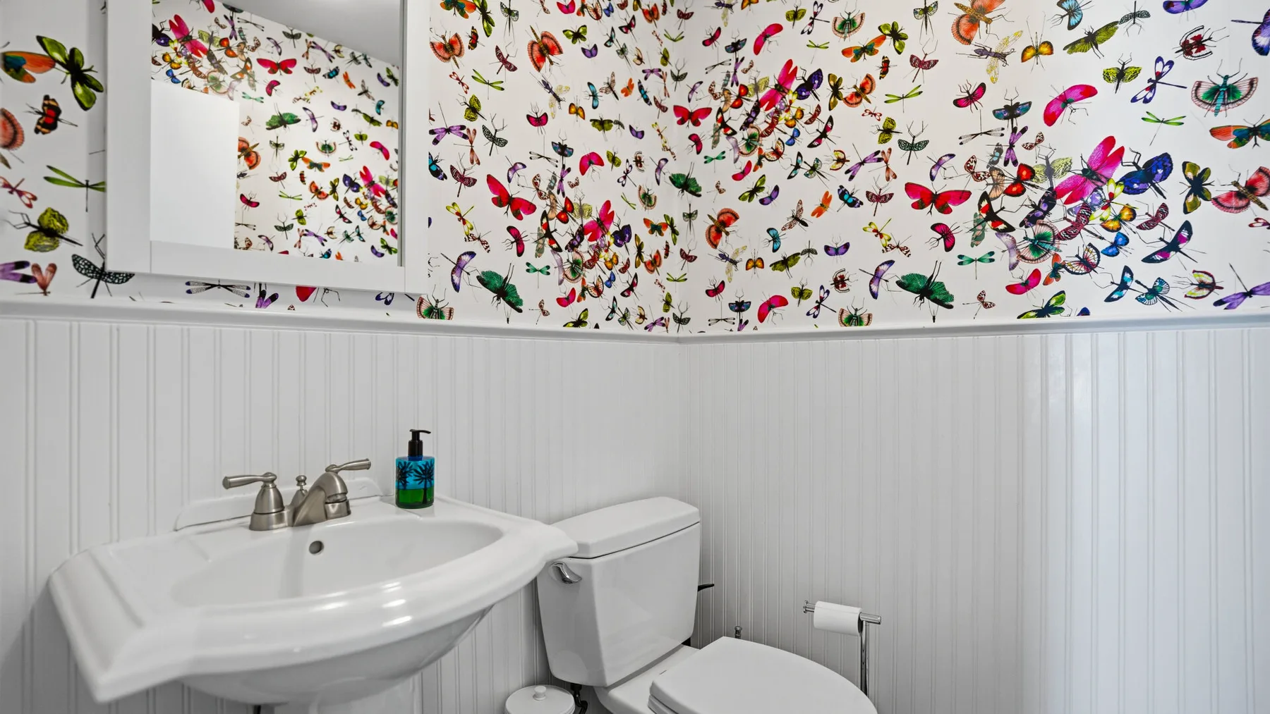 A bathroom with a sink and toilet beneath colorful insect-patterned wallpaper.