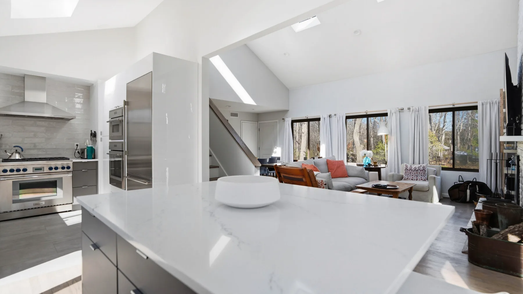 An open-plan kitchen and living area with a broad white island and seating by the windows.