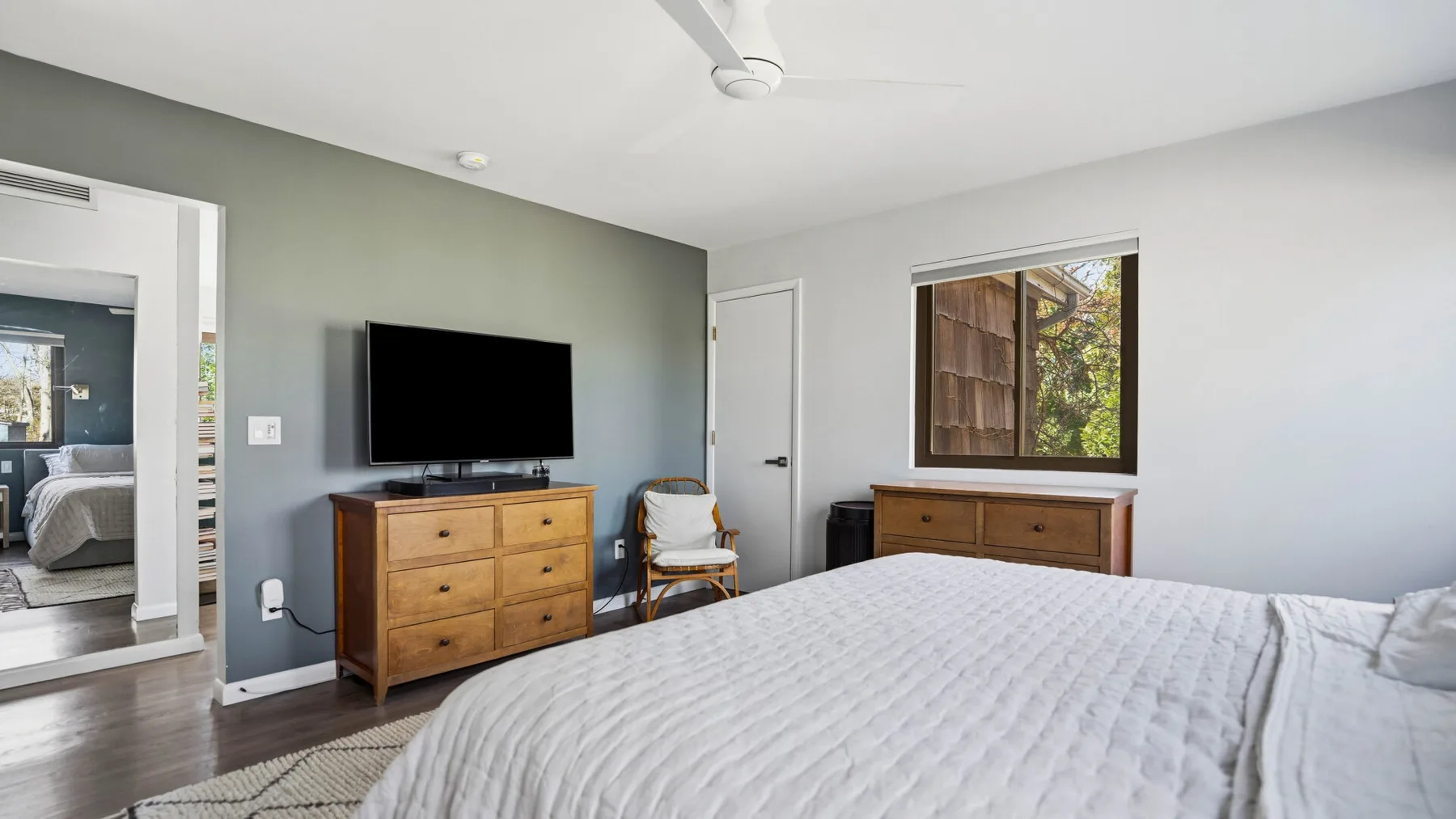 A bedroom with a bed, dresser, and television beside a window.