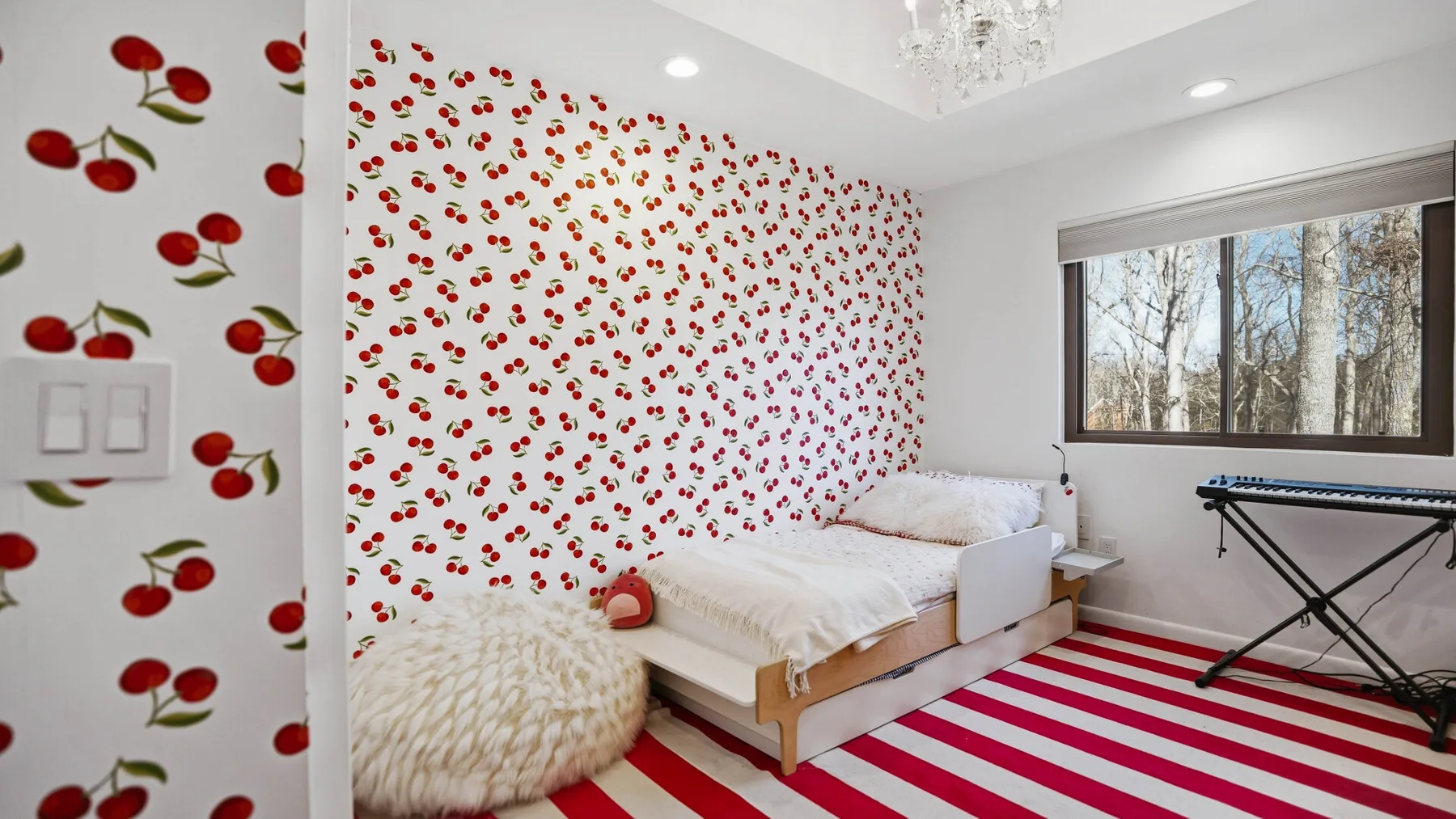 A bedroom with red-and-white striped flooring and cherry-patterned wallpaper.