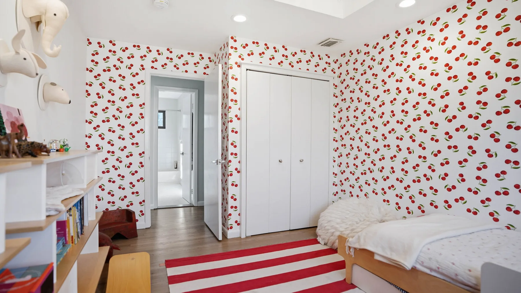 A bedroom with a bed, a white wardrobe, and red-and-white striped rug.