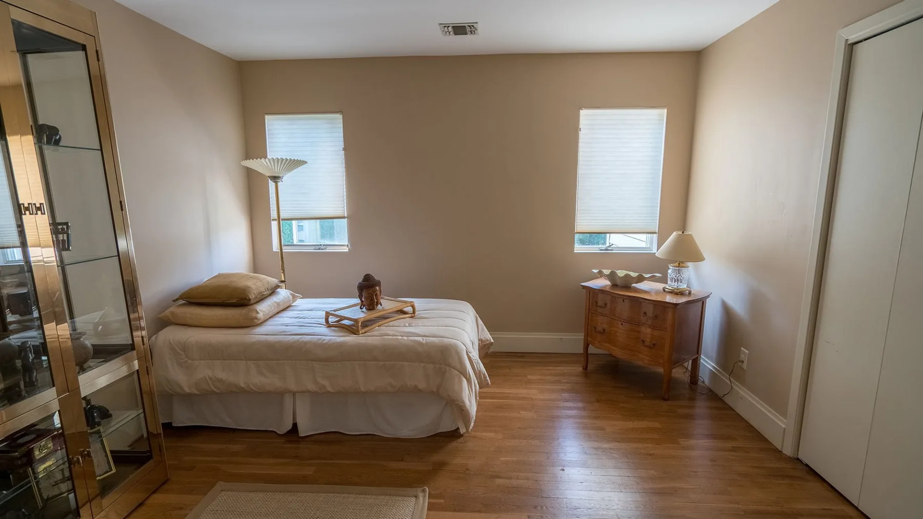 Un dormitorio con una cama, dos ventanas y una cómoda de madera.