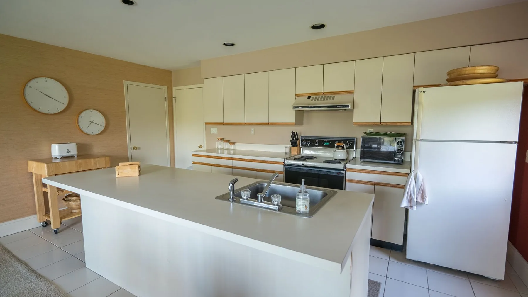 Una cocina luminosa con gabinetes claros, una isla grande y un refrigerador.