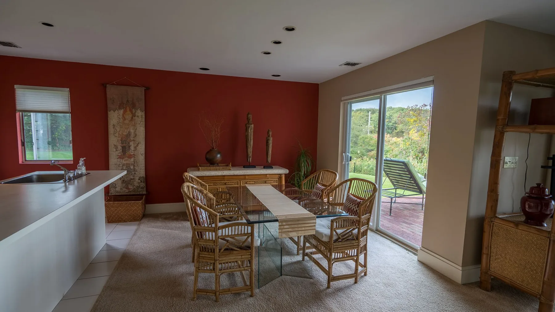 Comedor con mesa de vidrio y asientos de mimbre junto a grandes ventanas.