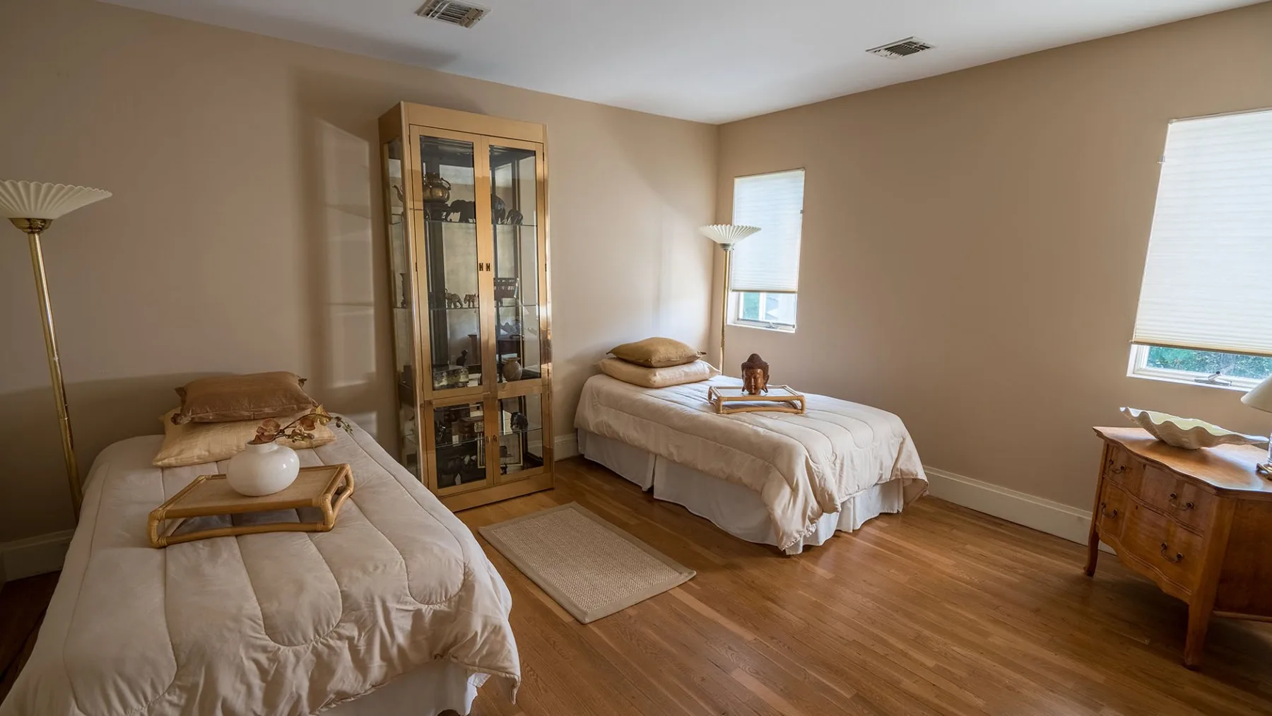 Un dormitorio con dos camas, un mueble con puertas de vidrio y suelo de madera.