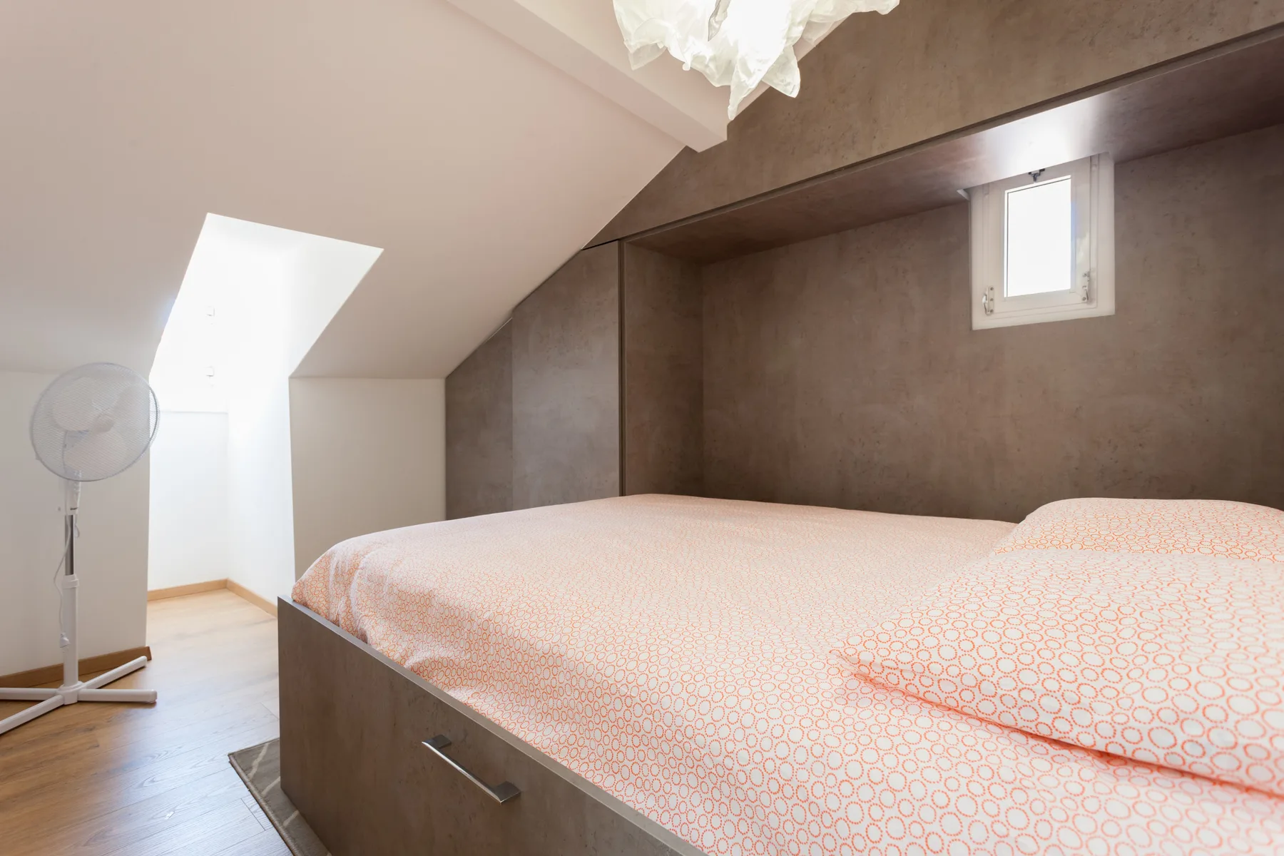 A bedroom with a bed beneath a sloped ceiling and a small window.