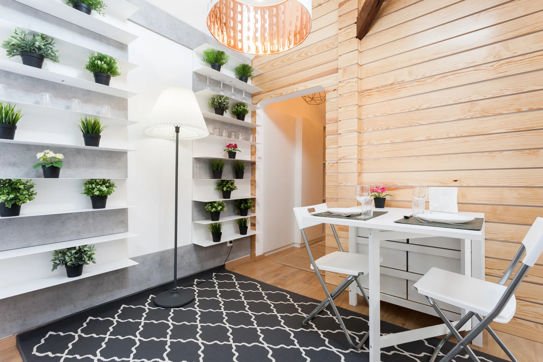Bright dining area with a white table, folding chairs, and wall shelves of plants.