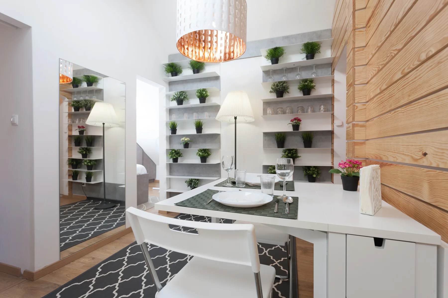 A dining area with a white table, chairs, and shelves of plants.