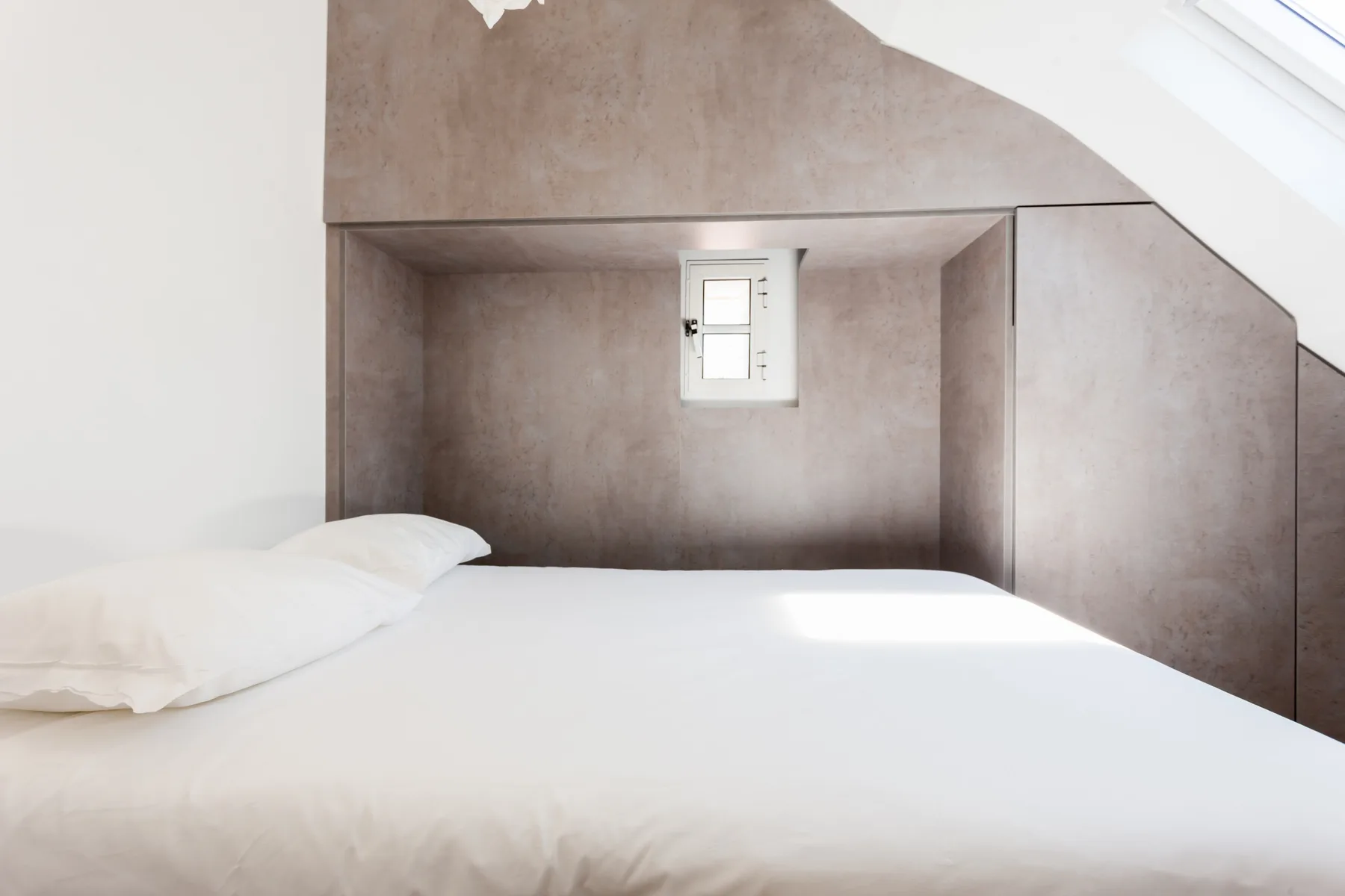 A bedroom with a bed tucked beneath a sloped ceiling and a small window.