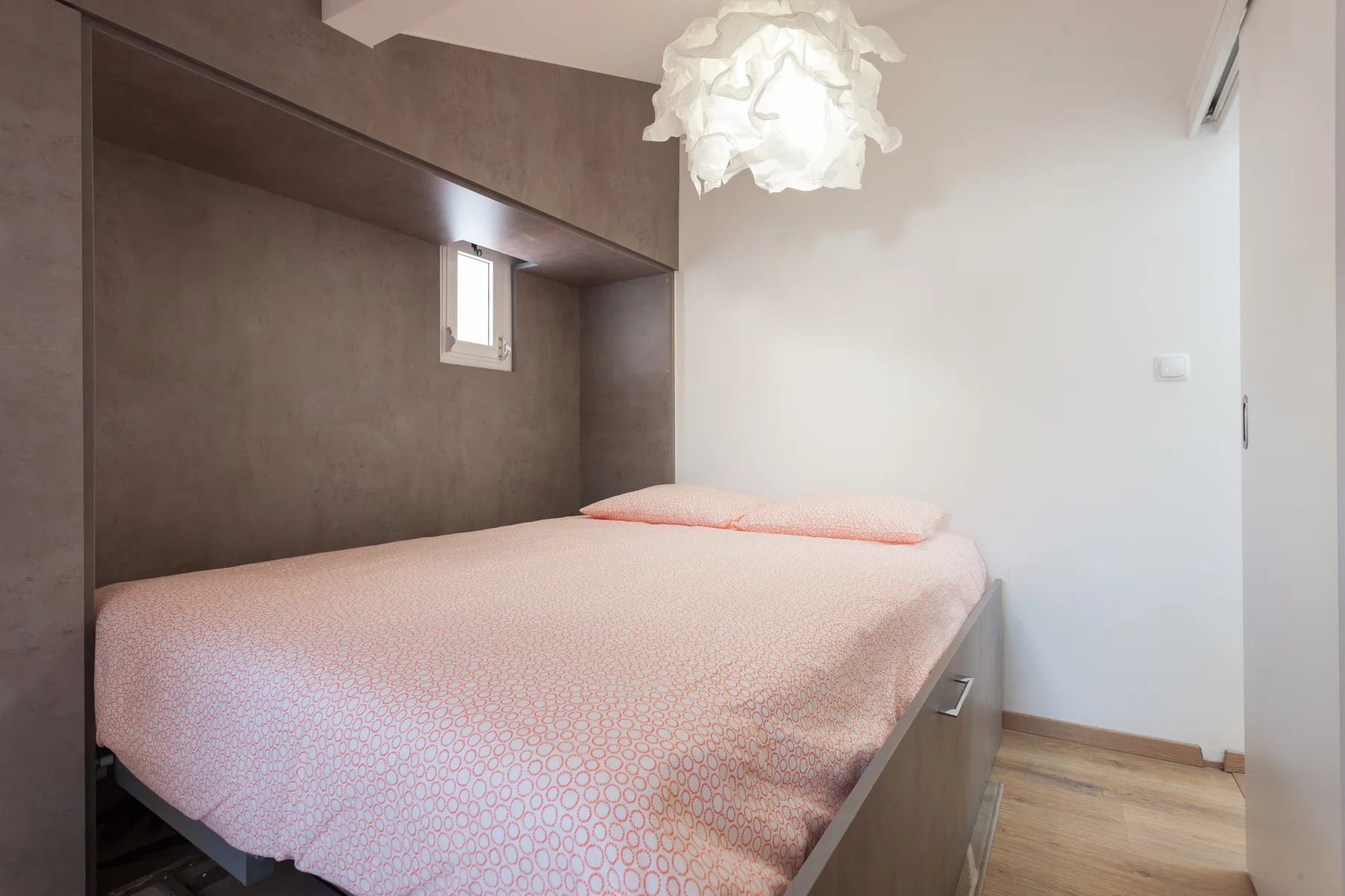 A bedroom with a bed covered in pale pink bedding beneath a hanging light.