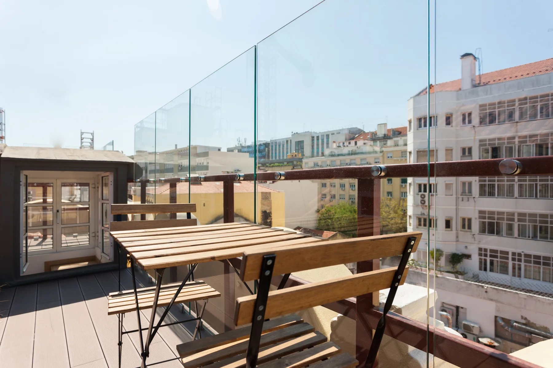 A rooftop terrace with outdoor seating and glass railings overlooking nearby buildings.
