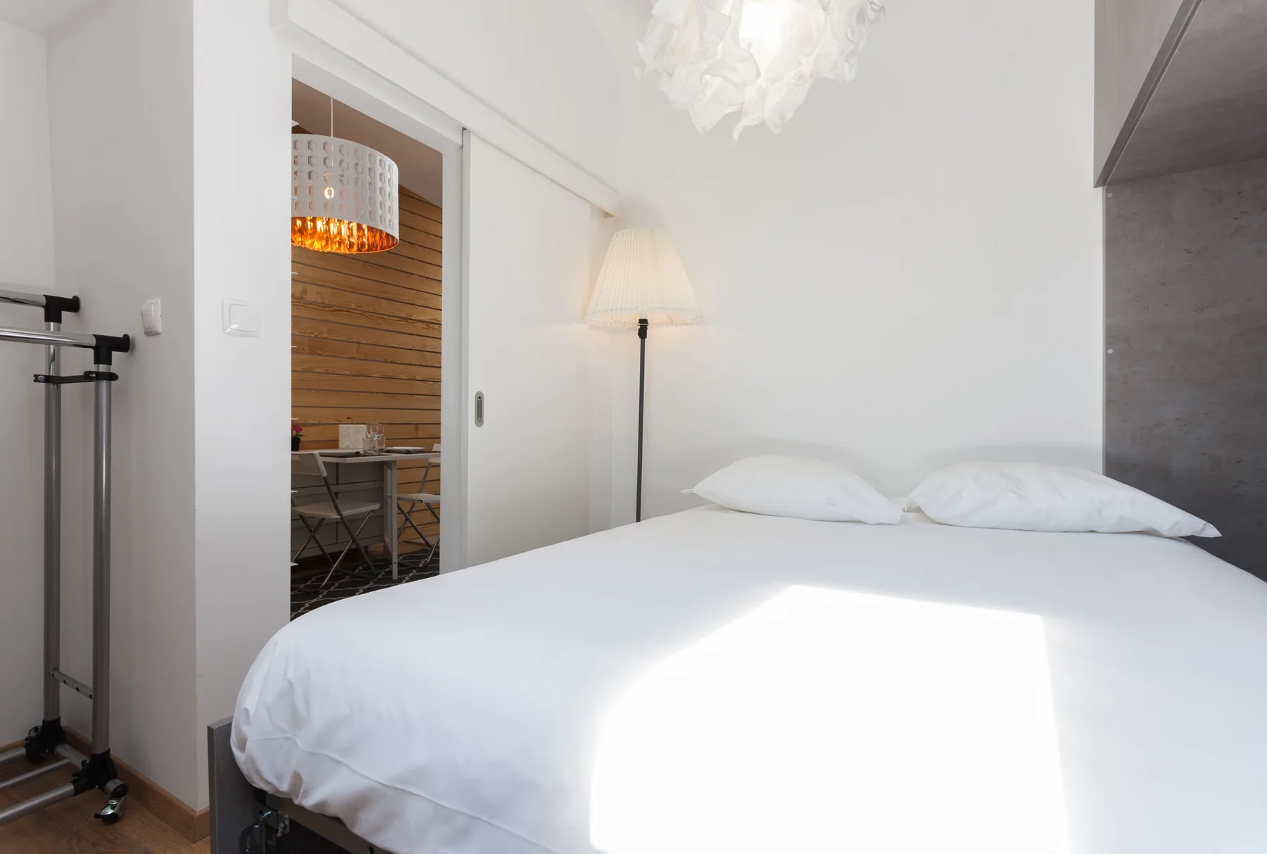 A bright bedroom with white bedding and a doorway opening to a dining area.