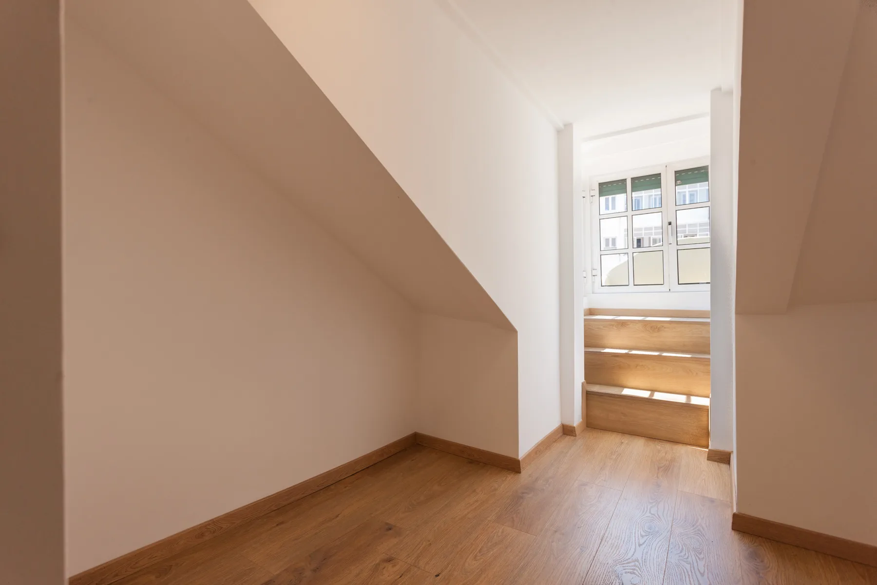 A small empty room with sloped walls and a window at the far end.