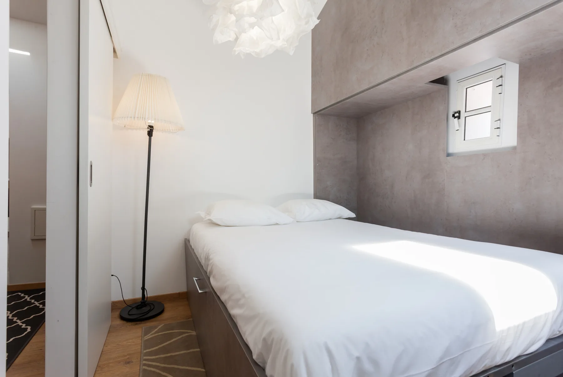 A bright bedroom with a neatly made bed and a floor lamp.