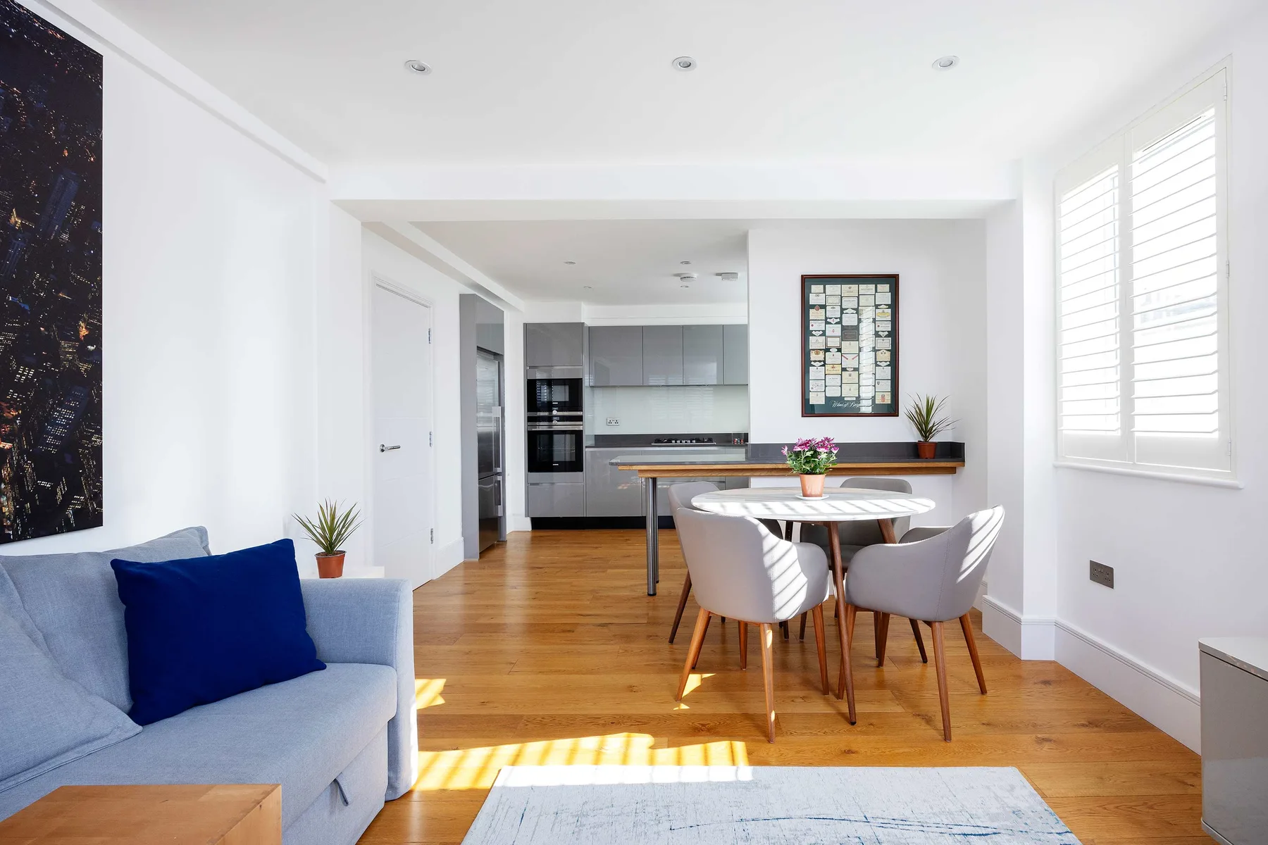 A bright open-plan living and dining area with a kitchen and sunlit windows.