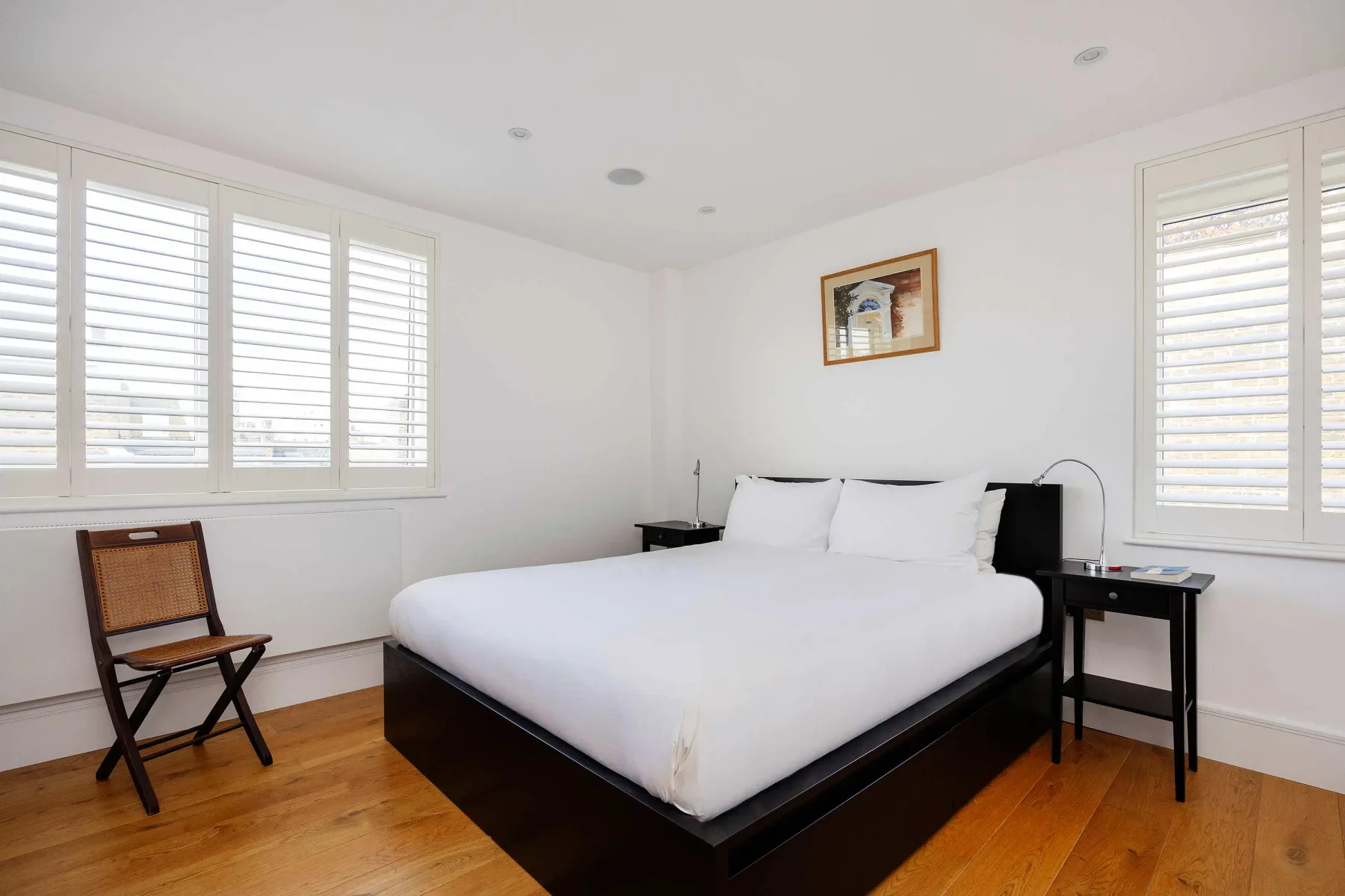 A bright bedroom with a large bed, white bedding, and shuttered windows.