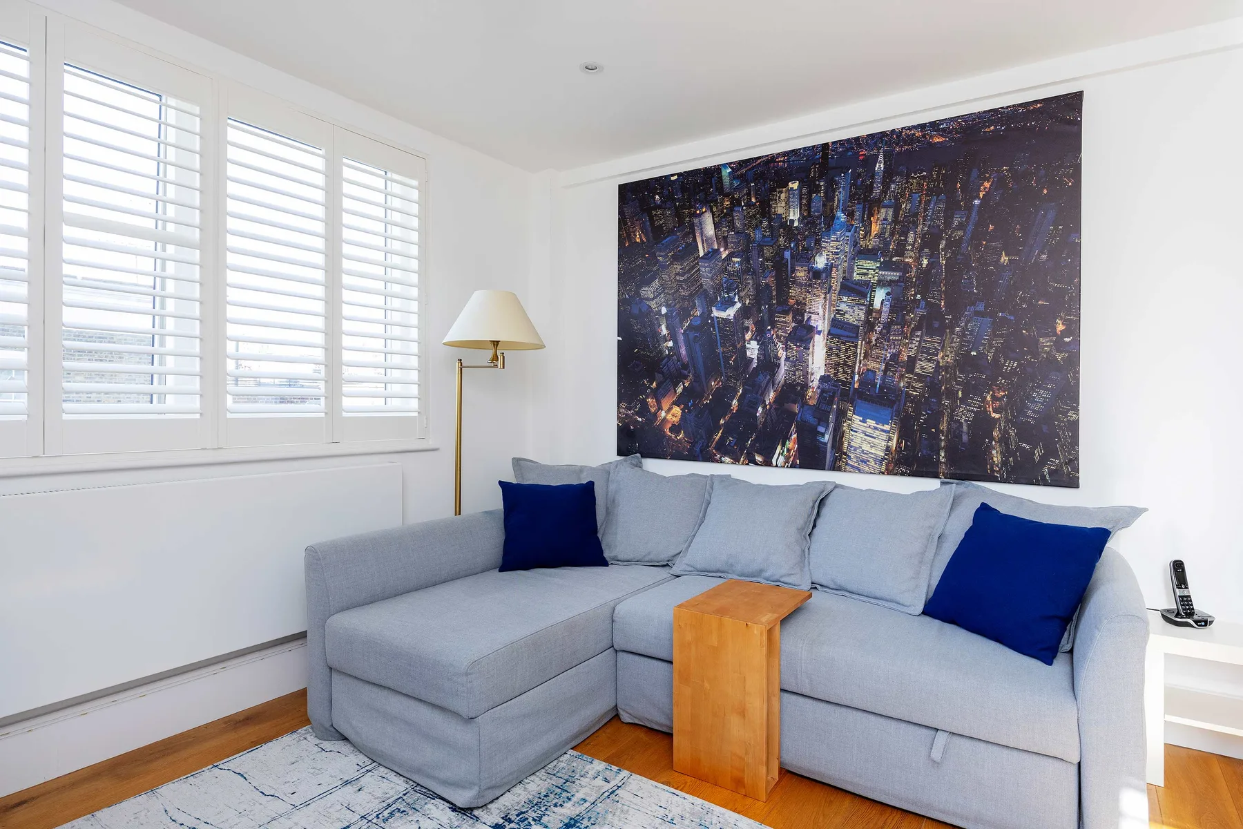 A bright living room with a gray sectional and a large cityscape artwork.